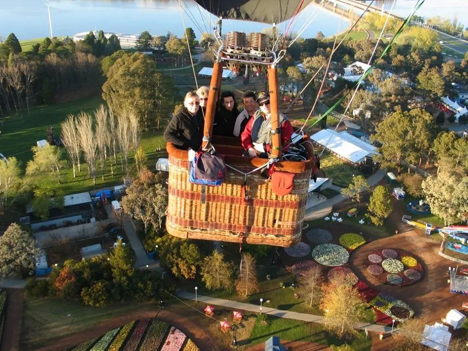 People riding in a hot air balloon over a park with colorful gardens.