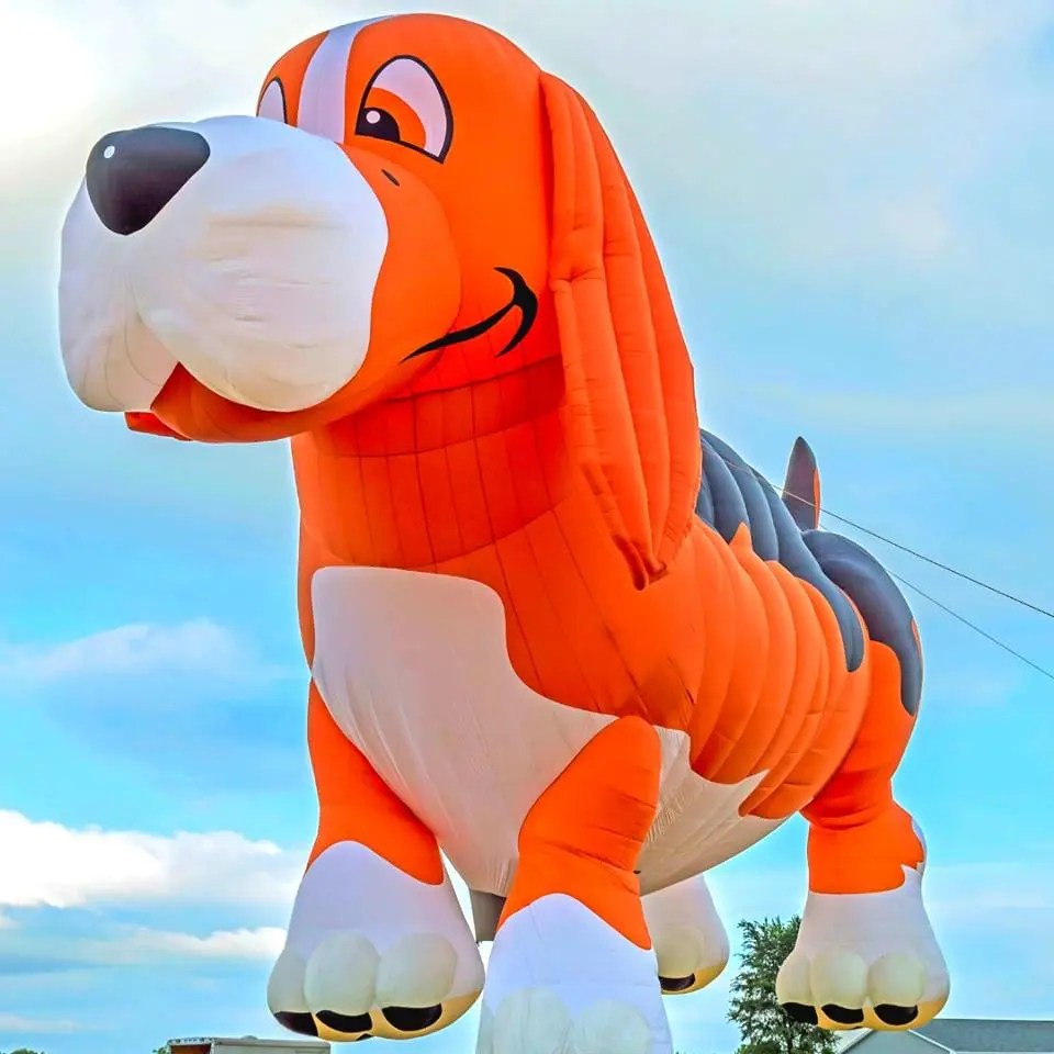 Large inflatable orange and white dog with long ears against a blue sky.
