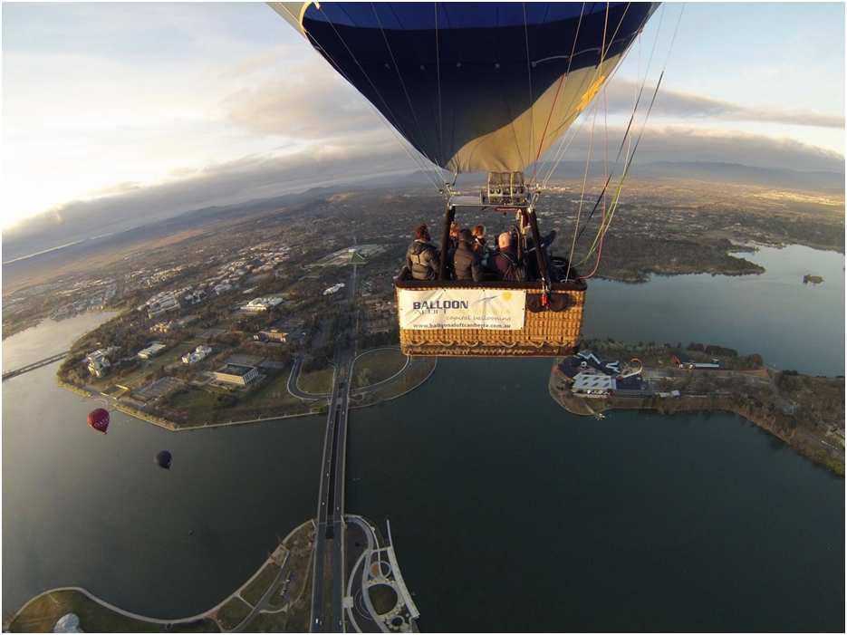 Hot air balloon with passengers flying over a lake and cityscape.