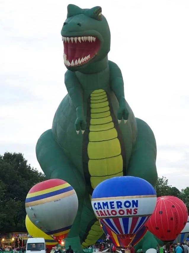 Giant green dinosaur balloon with smaller hot air balloons below it.