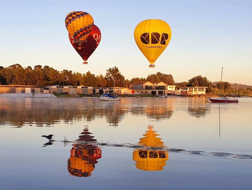 Two hot air balloons over a lake with a bird skimming the water.